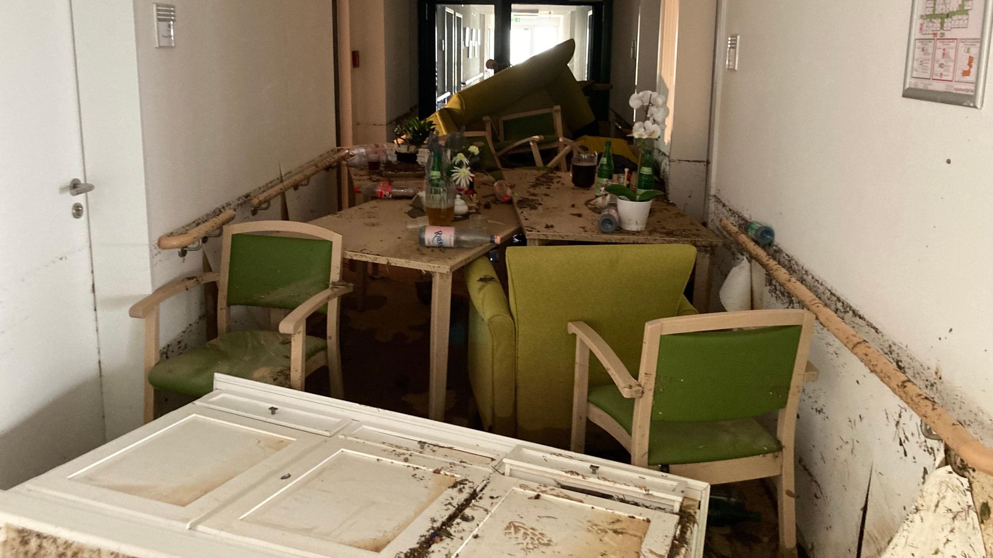 In einem schlammigen Flur sind beschädigte Möbel gestapelt.
