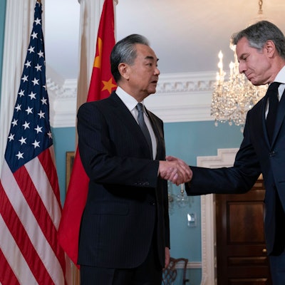 Zwei Männer in Anzügen schütteln sich die Hand. Im Hintergrund befinden sich amerikanische Flaggen sowie eine chinesische Flagge.