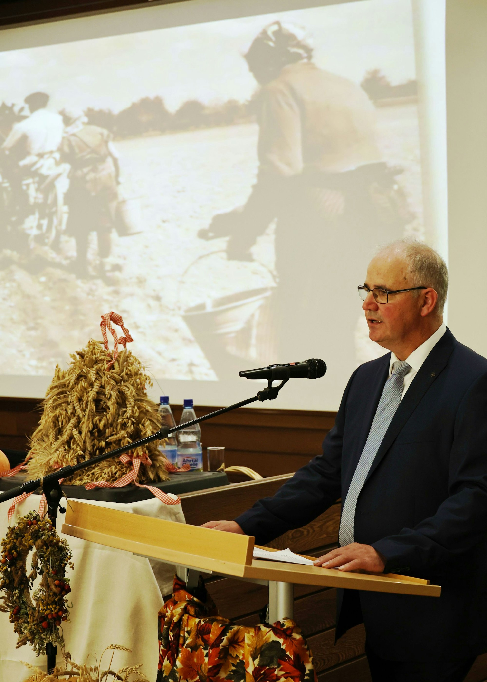 Helmut Dahmen bei seiner Rede, im Hintergrund die Projektion von Bäuerinnen auf einem Feld.
