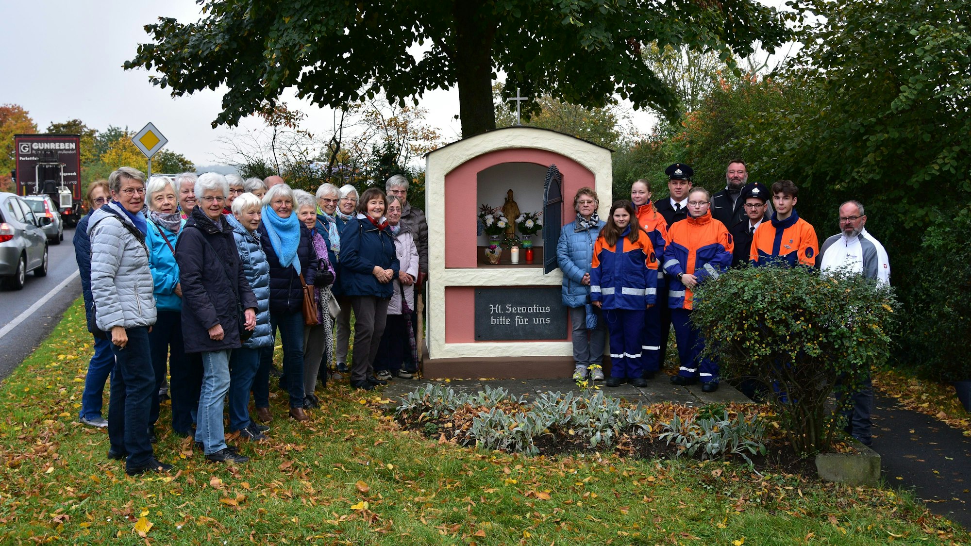 Kleines Häuschen an einer Verkehrsstraße mit einer Menschenmenge drumherum.