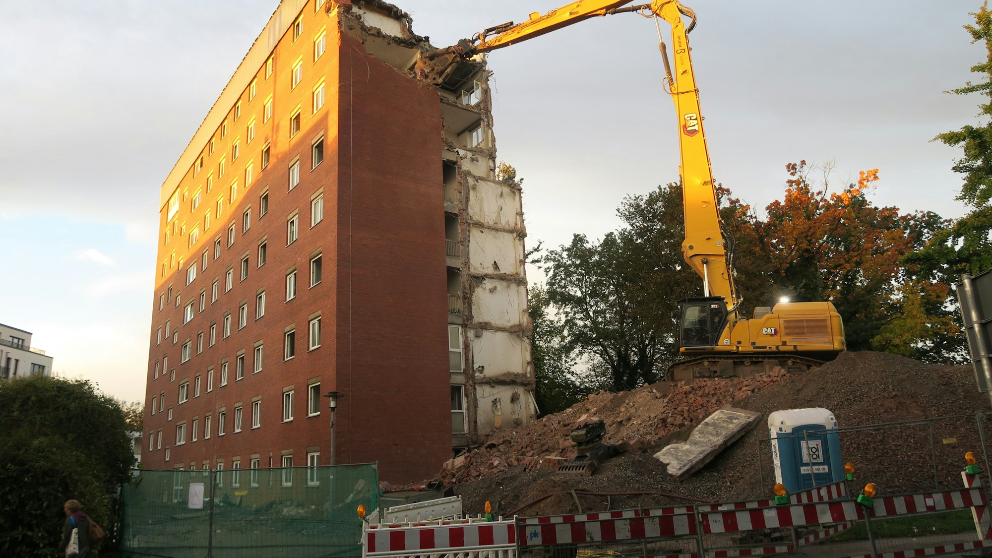Ein Bagger, der auf einem Erdhügel steht hat seine Schaufel in die oberste Etage eines etwa zehnstöckigen Hochhauses geschlagen.