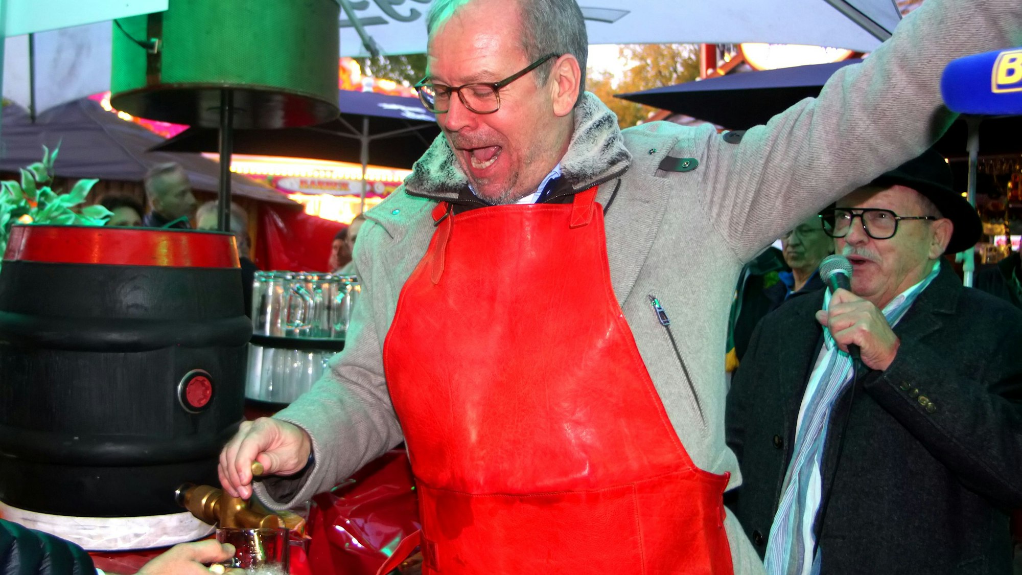 Ein Mann mit roter Schürze und Brille schlägt den Zapfhahn in ein Bierfass.