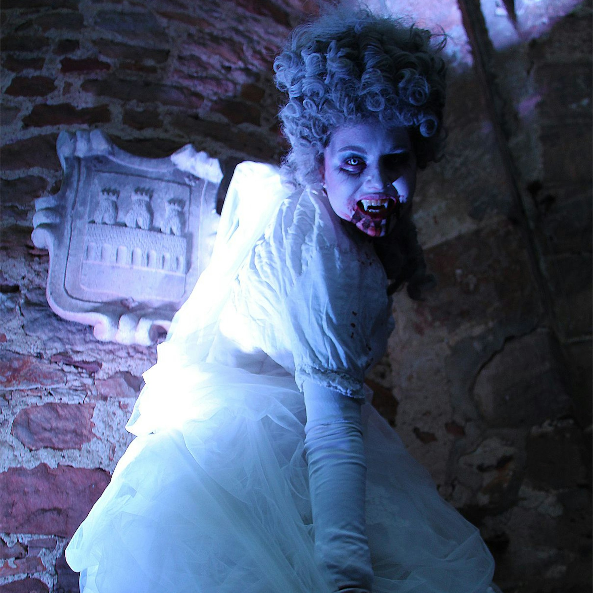 Die weiß gekleidete Vampirfrau bleckt ihre spitzen Zähne.