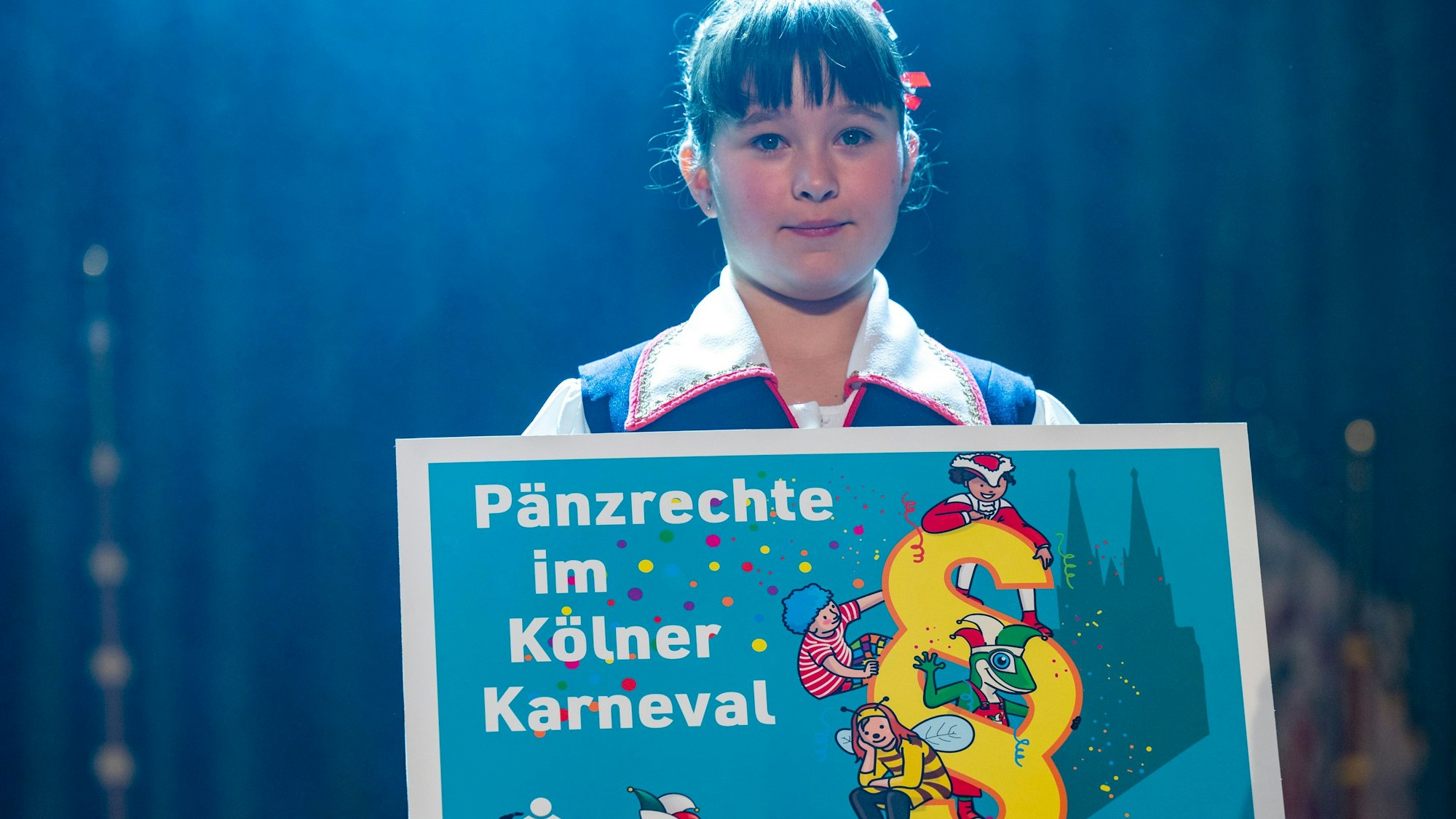 Ein Mädchen hält ein Schild mit dem Titel „Pänzrechte im Kölner Karneval“ in der Hand.