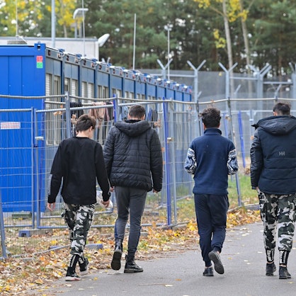 Vier Jugendliche sind von hinten zu sehen, daneben stehen Container für Geflüchtete