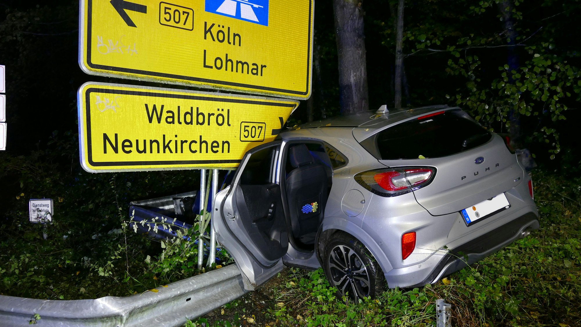 Ein zerstörtes Auto vor einem großen Straßenschild.