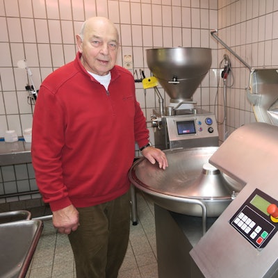 Ein alter Herr im roten Pullover steht neben einer Maschine aus Edelstahl.