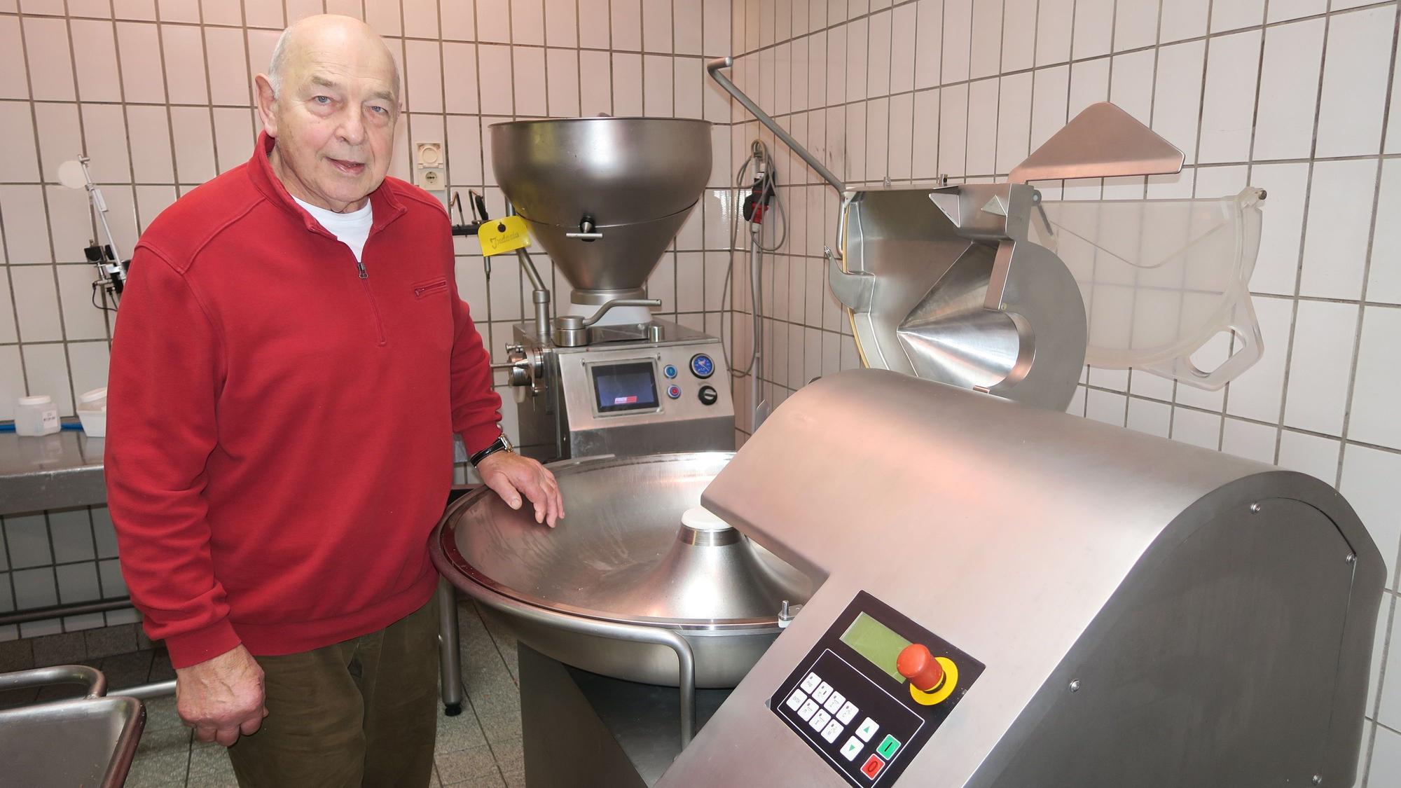 Ein alter Herr im roten Pullover steht neben einer Maschine aus Edelstahl.