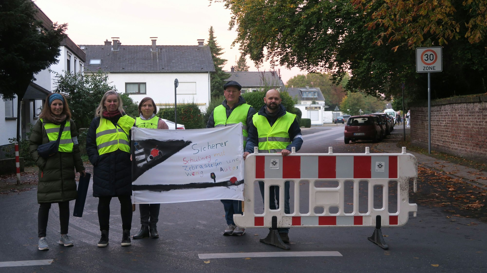 Fünf Personen mit gelben Warnwesten halten ein Transparent hoch. Sie stehen neben einer Absperr-Bake.