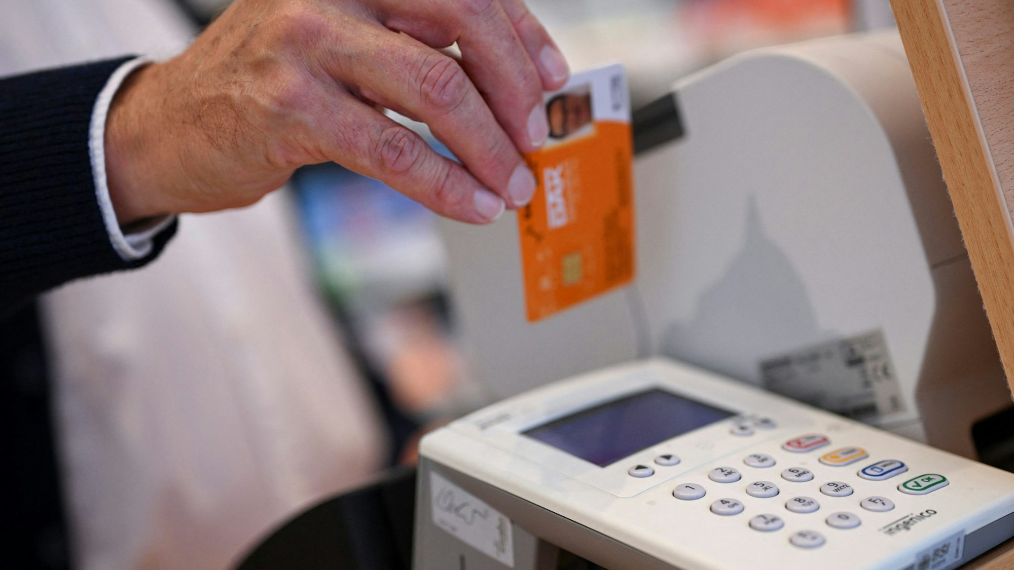 Eine Person legt die Gesundheitskarte eines Patienten in ein Kartenlesegerät in einer Apotheke.