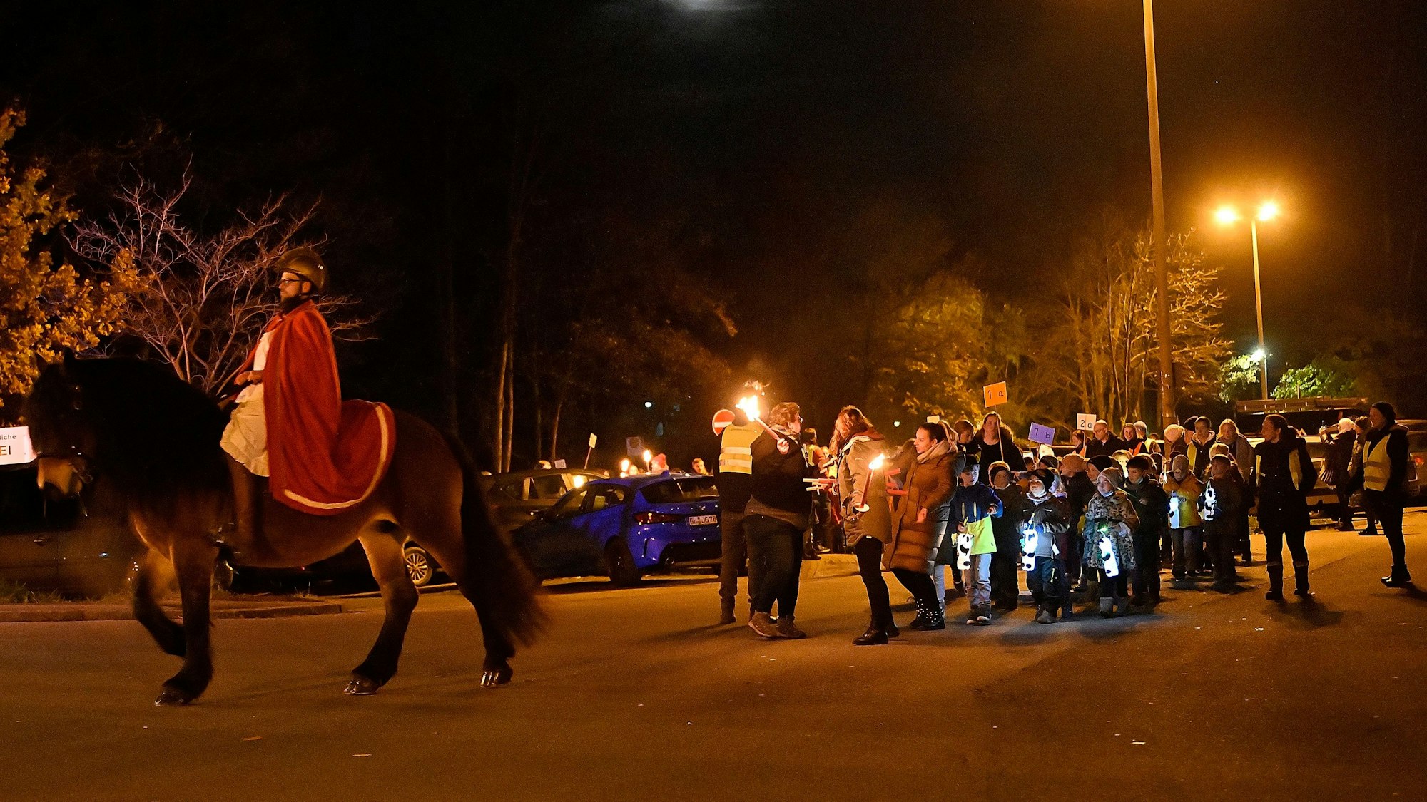 Ein St.-Martin-Darsteller reitet auf einem Pferd vor einem Zug von Kindern und Erwachsenen mit Laternen und Fackeln in Kürten.