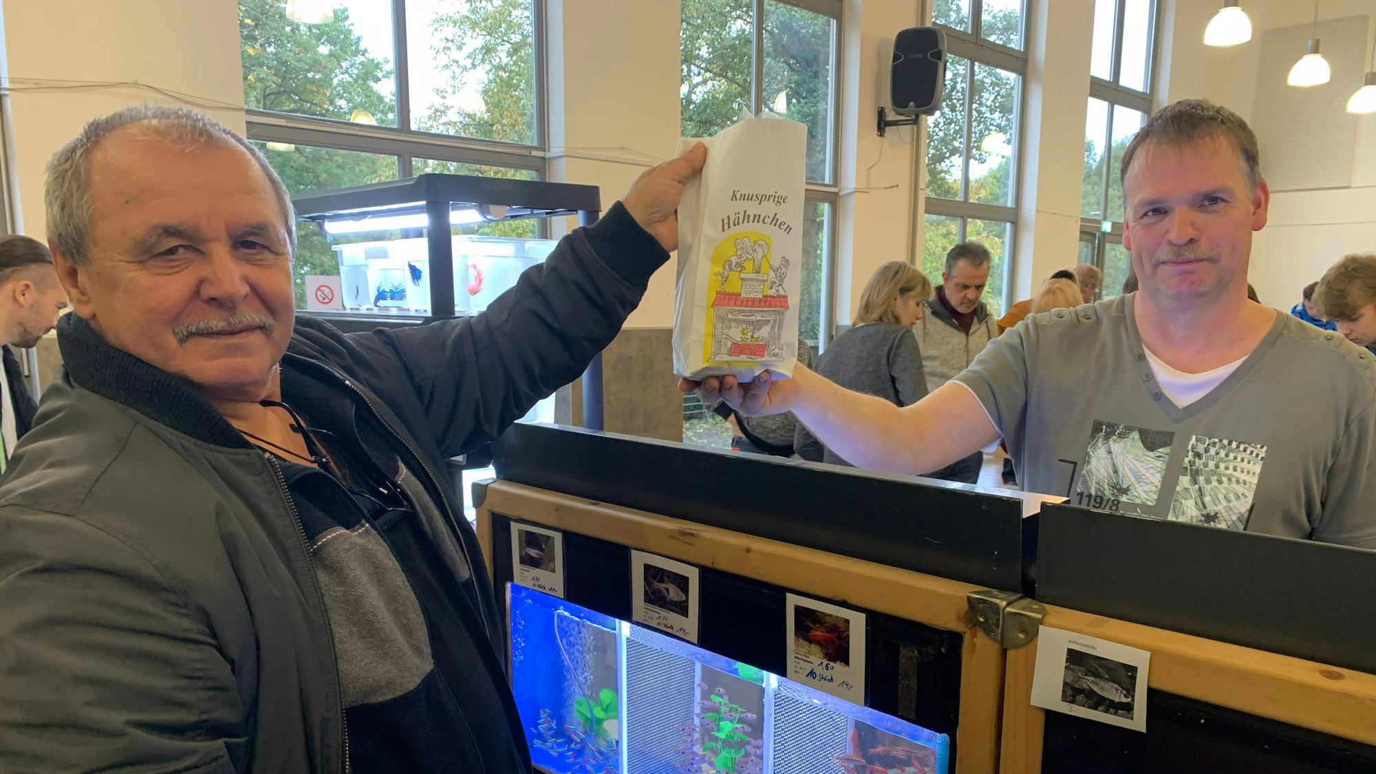 Ein Käufer nimmt gekaufte Fische entgegen, die sich in einer Hähnchentüte befinden. So wurde auf der Aquarien-Börse des Aquarien- und Terrarien-Verein Nymphea-Siegburg verkauft.