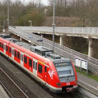 Eine S-Bahn steht an einer Haltestelle, die durch eine Fußgängerbrücke erreichbar ist.
