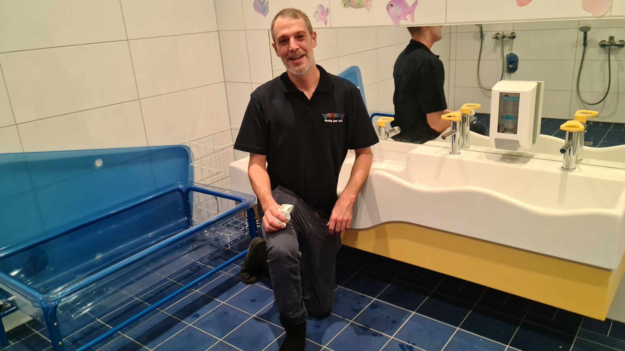 Ein Mann steht in einem kindgerechten Badezimmer mit einem großen niedrigen Waschbecken.