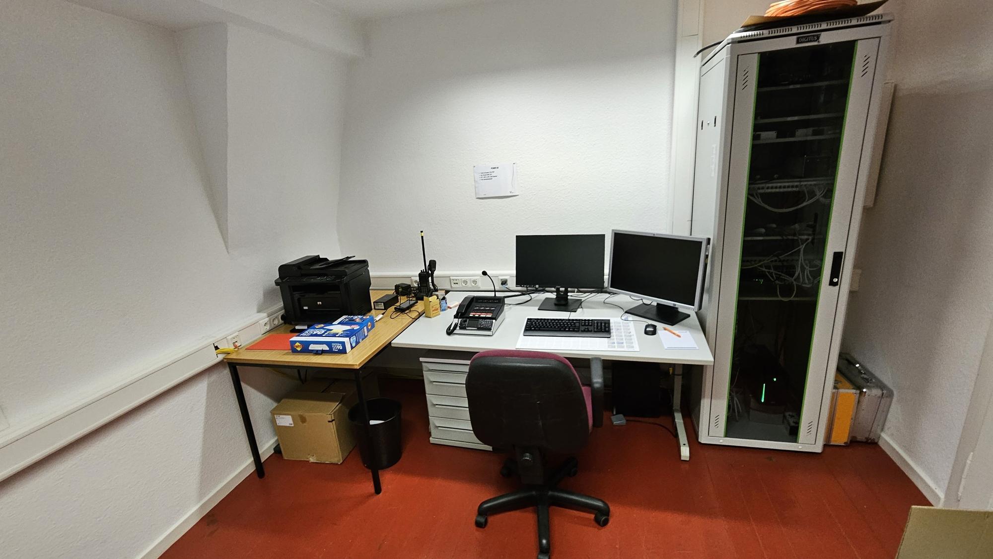 Blick in ein Büro mit Schreibtisch, zwei Bildschirmen und Funkverbindung.