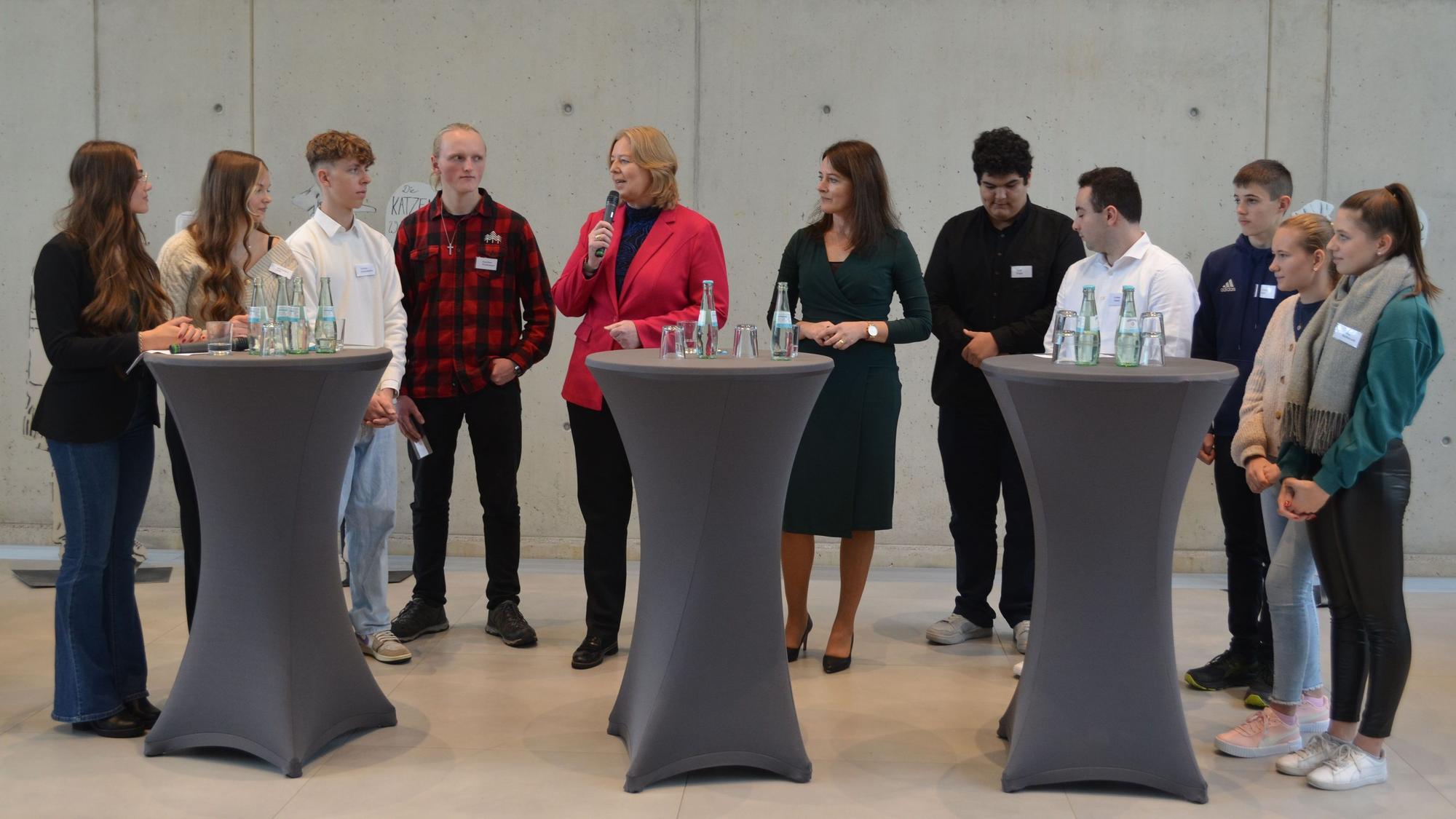 Bundestagspräsidentin Bärbel Bas mit Schülern an Stehpulten.