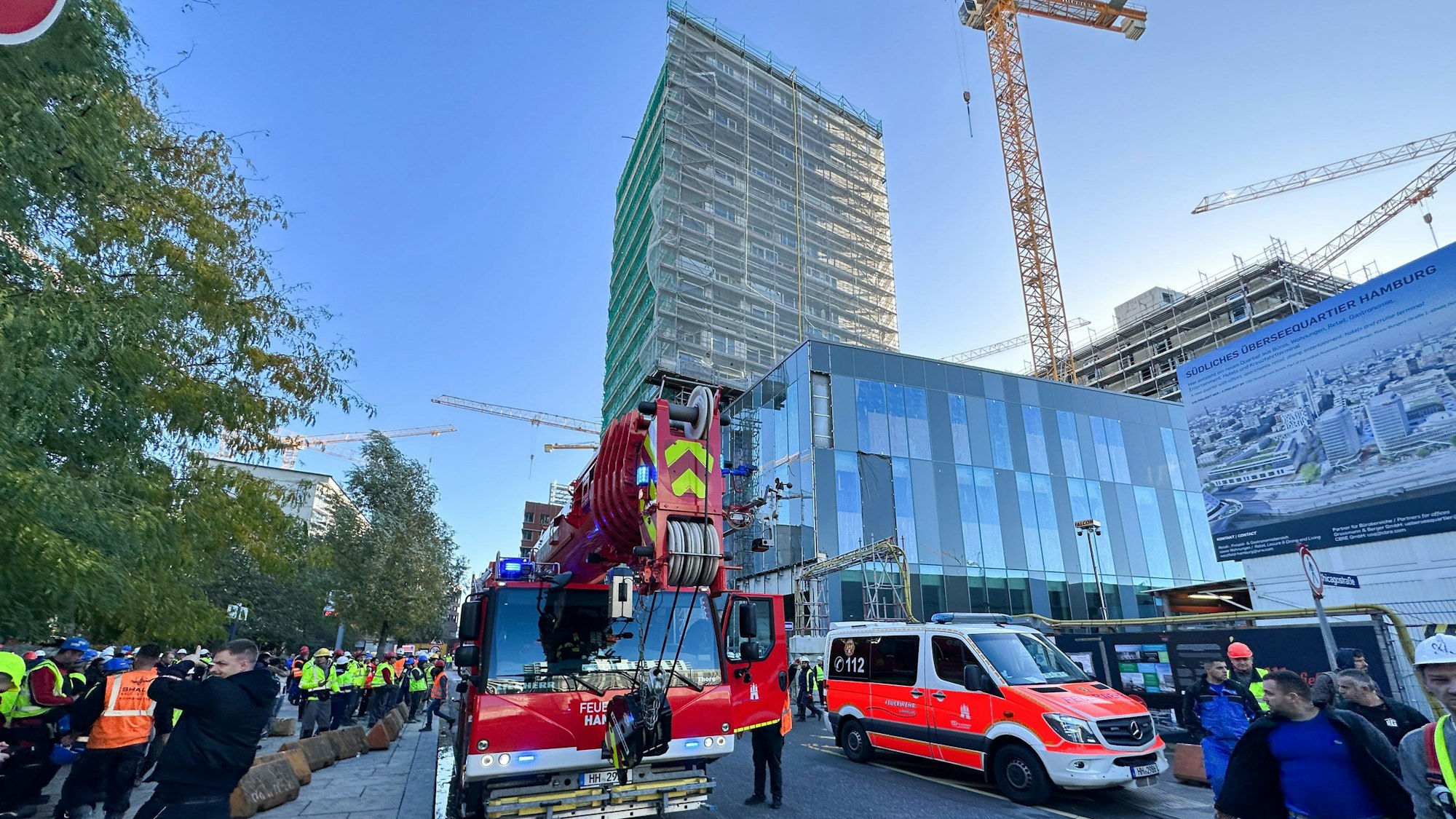 Einsatzfahrzeuge der Feuerwehr stehen vor einem eingerüsteten Hochhaus.
