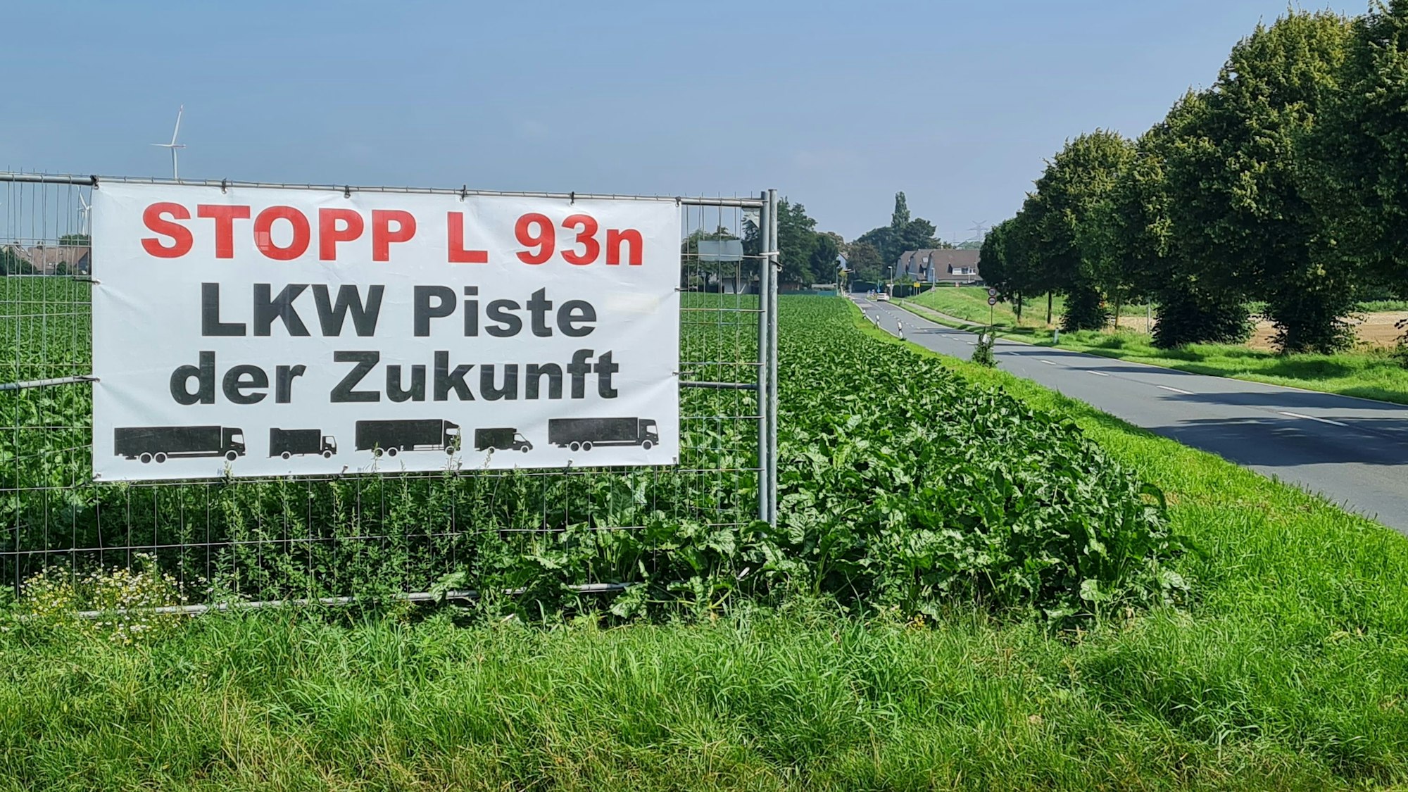 Ein Transparent mit der Aufschrift „Stopp L 93n, Lkw-Piste der Zukunft“ hängt an einem Bauzaun auf einem Feld neben einer Straße.
