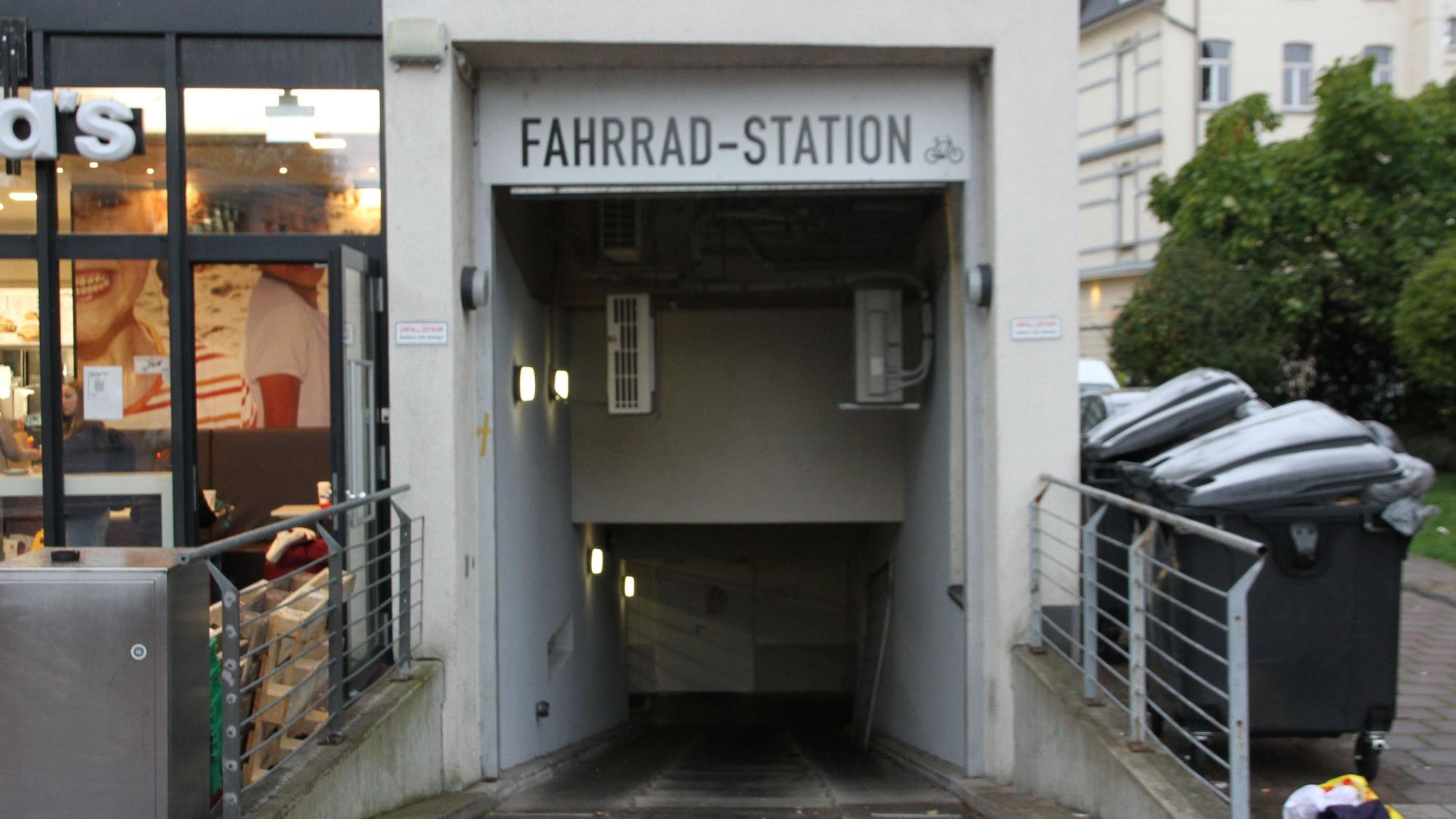 Eingang zu einer Fahrrad-Tiefgarage zwischen einem Schnellimbiss und Müllcontainern