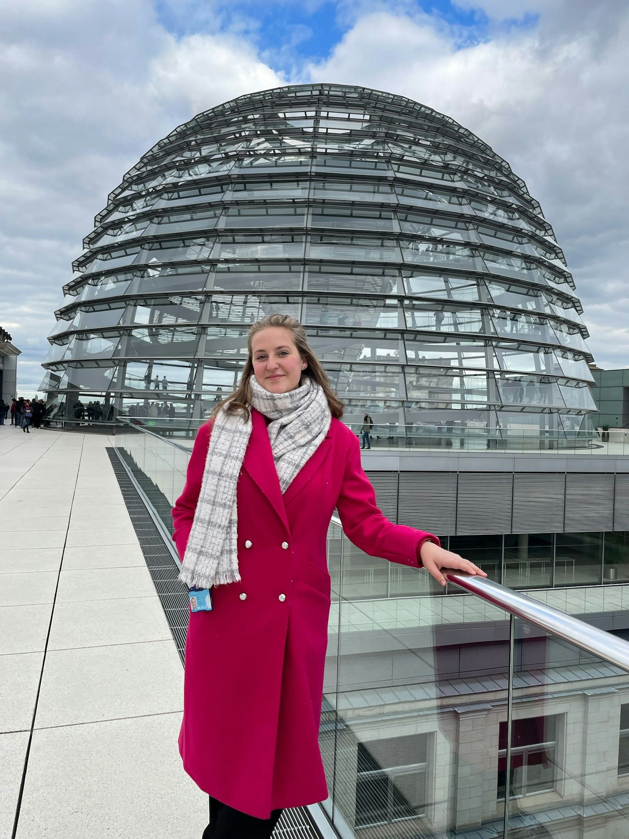 Madita Ehrhardt steht in einem roten Mantel auf der Dachterrasse des Deutschen Bundestags, im Hintergrund die Reichstagskuppel.