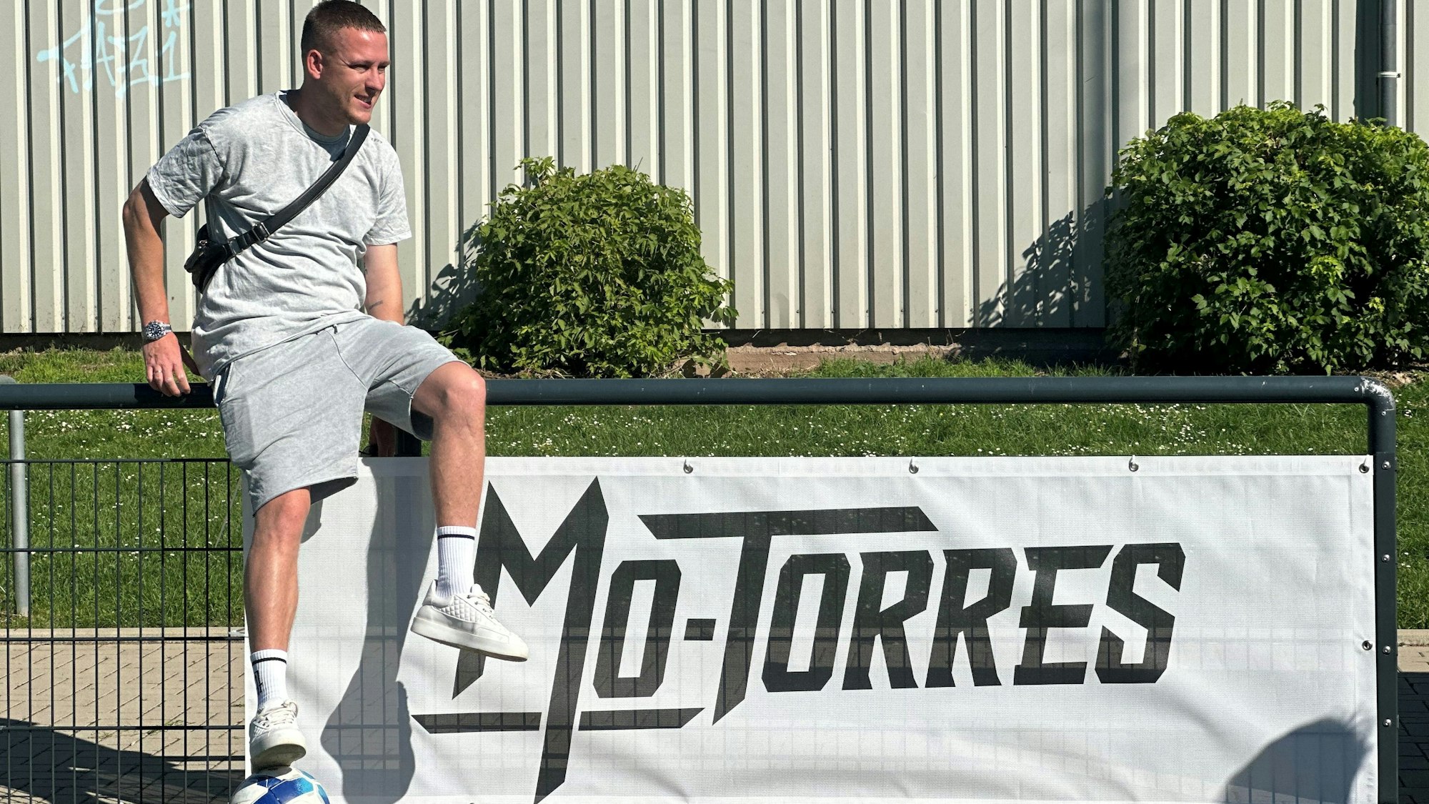 Ein junger Mann sitzt auf einem Zaun, an dem das Banner mit der Aufschrift Mo-Torres befestigt ist.