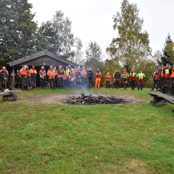 Jäger, Treiber und Jagdhornbläser stehen um ein Lagerfeuer.