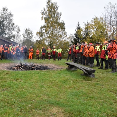 Jäger, Treiber und Jagdhornbläser stehen um ein Lagerfeuer.