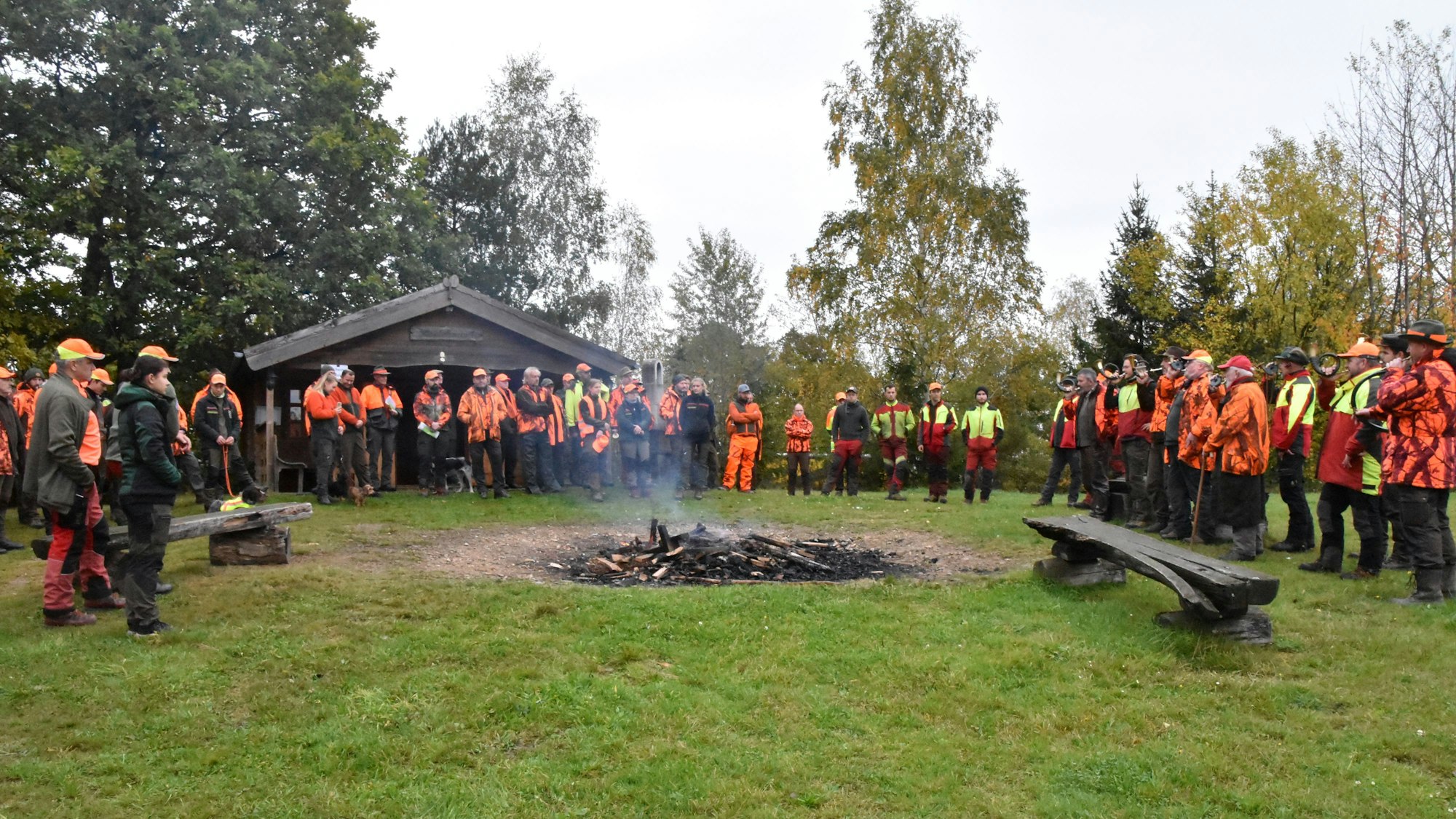 Jäger, Treiber und Jagdhornbläser stehen um ein Lagerfeuer.