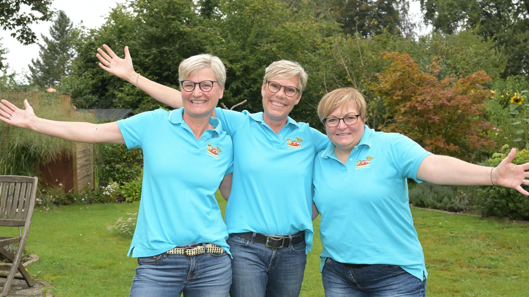 Die angehenden Refrather Tollitäten des Frauendreigestirns stehen im Garten, haken sich unter und strecken die Arme in die Höhe.