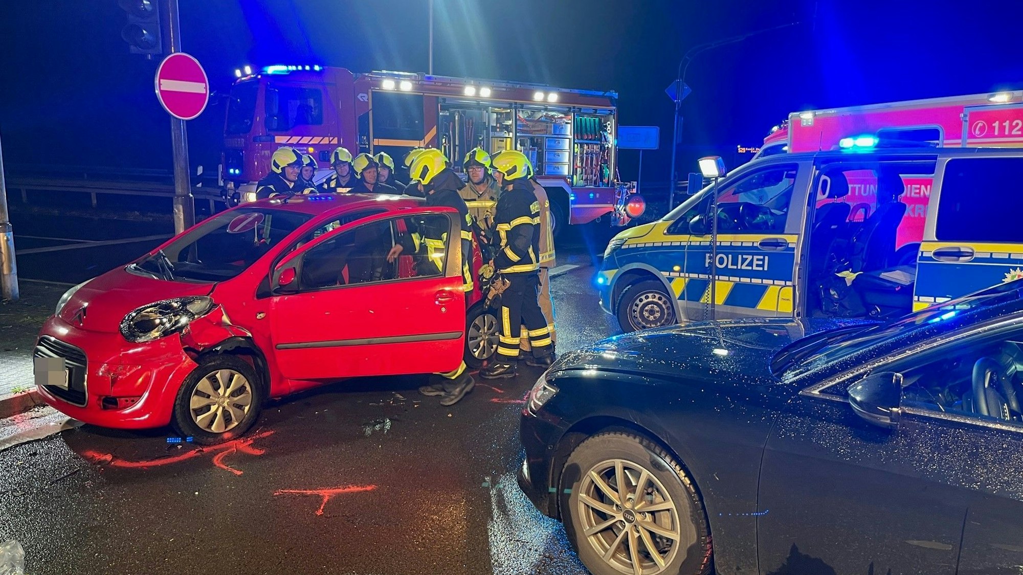 Feuerwehrleute und die Polizei stehen an zwei beschädigten Autos.