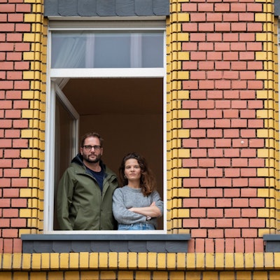 Lynn Busch und Hannes Kleinknecht stehen am geöffneten Fenster ihrer Wohnung in Ehrenfeld. Am Fenster rechts ist eine israelische Flagge zu sehen.