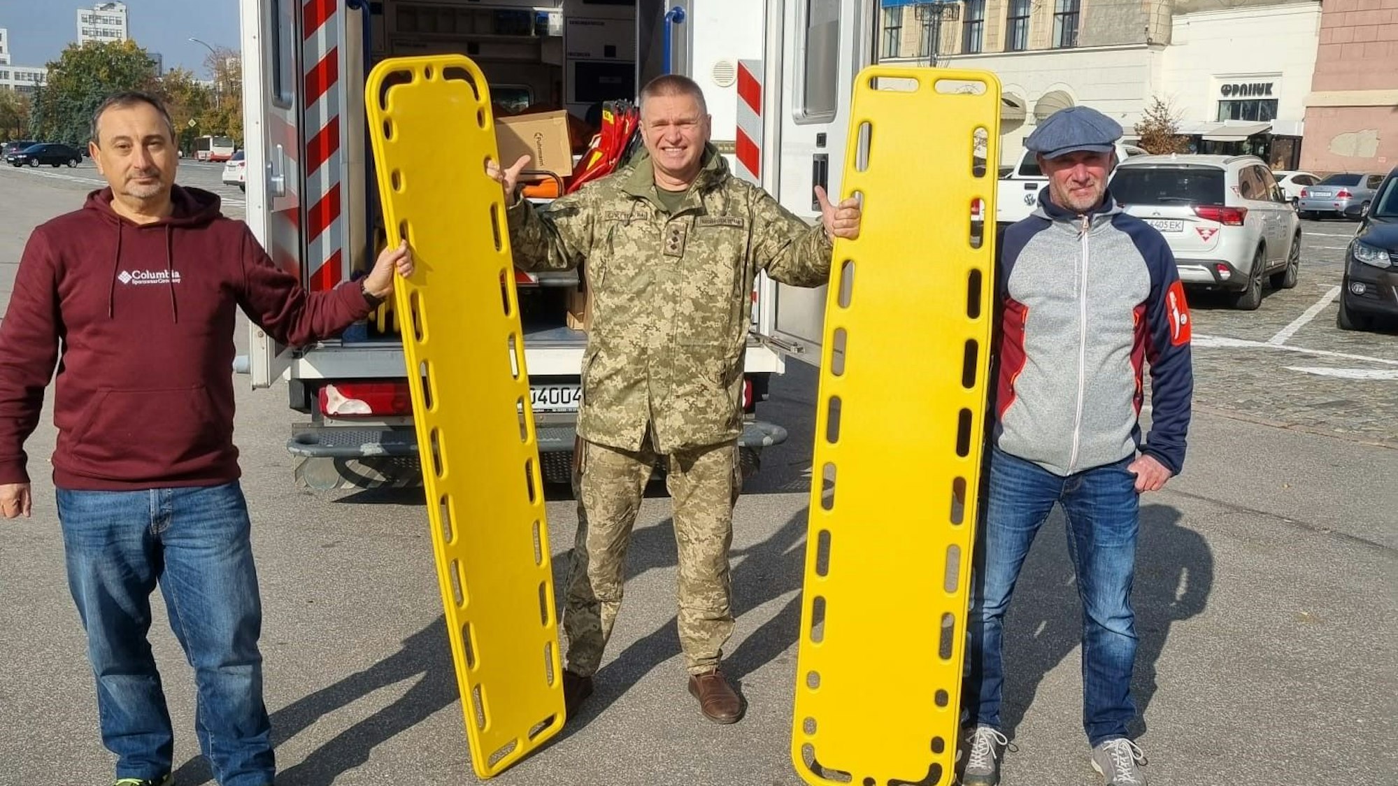 Drei Männer stehen vor einem Krankenwagen mit gelben Trageliegen.