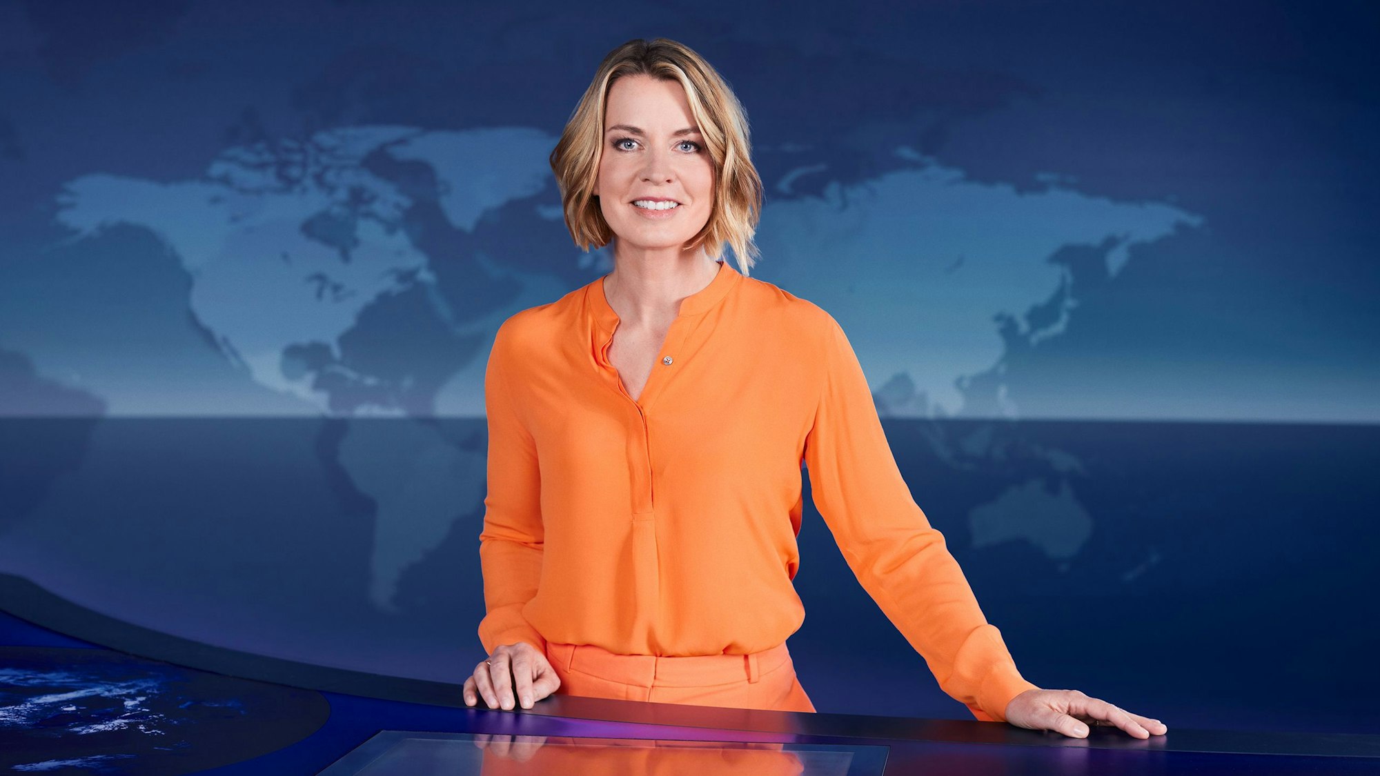 Tagesthemen-Moderatorin Jessy Wellmer steht im ARD-Nachrichtenstudion in Hamburg und schaut in die Kamera. Sie trägt eine orangefarbene Hose und ein orangefarbenes Oberteil.