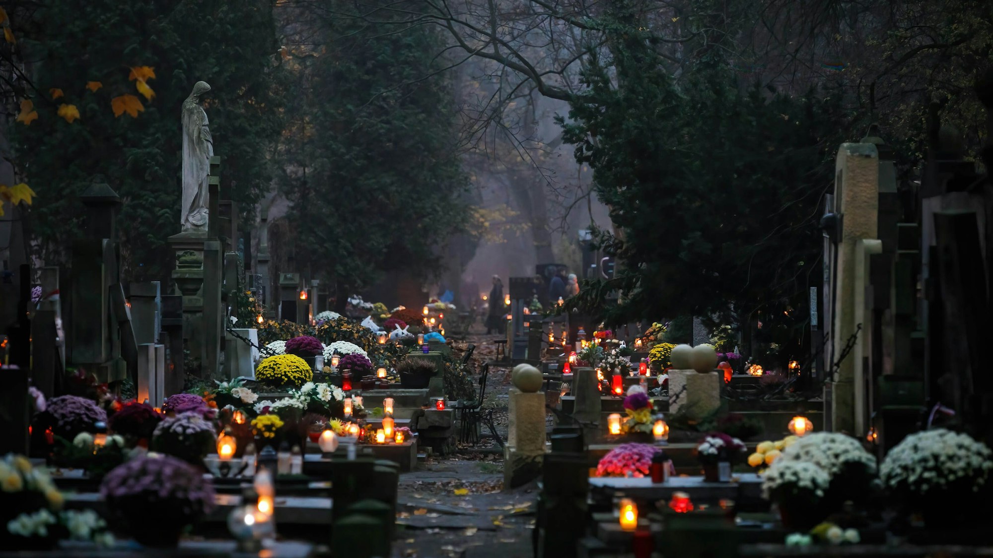 Brennenden Kerzen und Blumen schmücken eine Reihe von Gräbern.