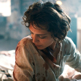 Orta sitzt auf ihrem Bett und schaut nach unten. Ihre Kleidung ist voller Blut. Der Hintergrund ist verschwommen, man erkennt ihre Wohnung, ihren toten Freund im Bett.