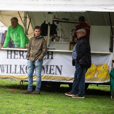 Das Bild zeigt zwei Fans, die dem Regen beim kleinen Pokalfinale trotzen. Sie stehen an einer Bierbude.