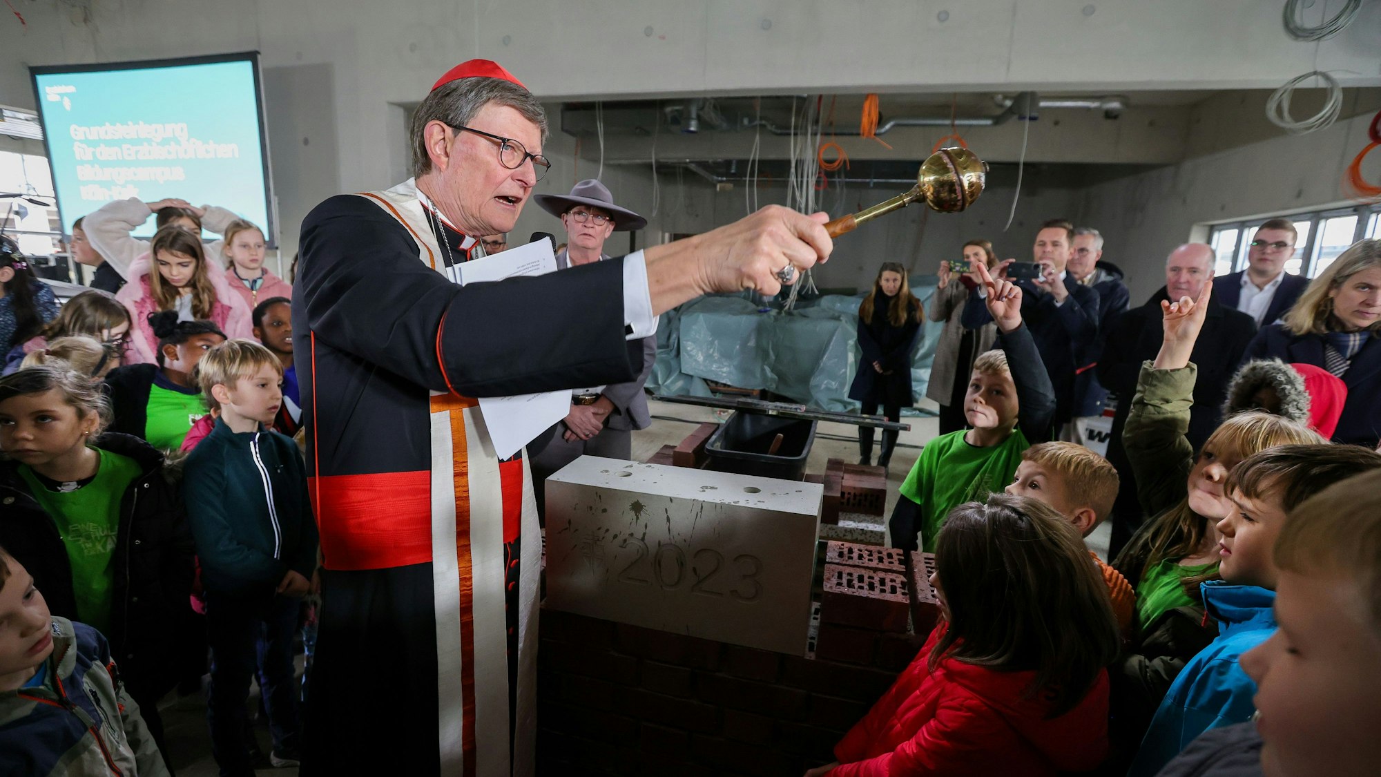 Rainer Maria Woelki segnet den Grundstein, viele Kinder stehen um ihn herum.