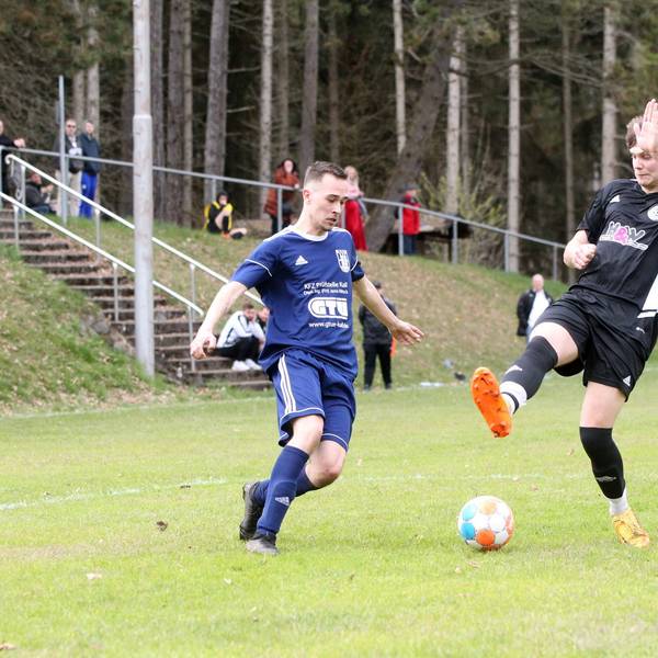 Maurice Gölden versucht sich den Ball am mit gestrecktem Bein heraneilendem Stotzheimer Spieler vorbeizulegen.