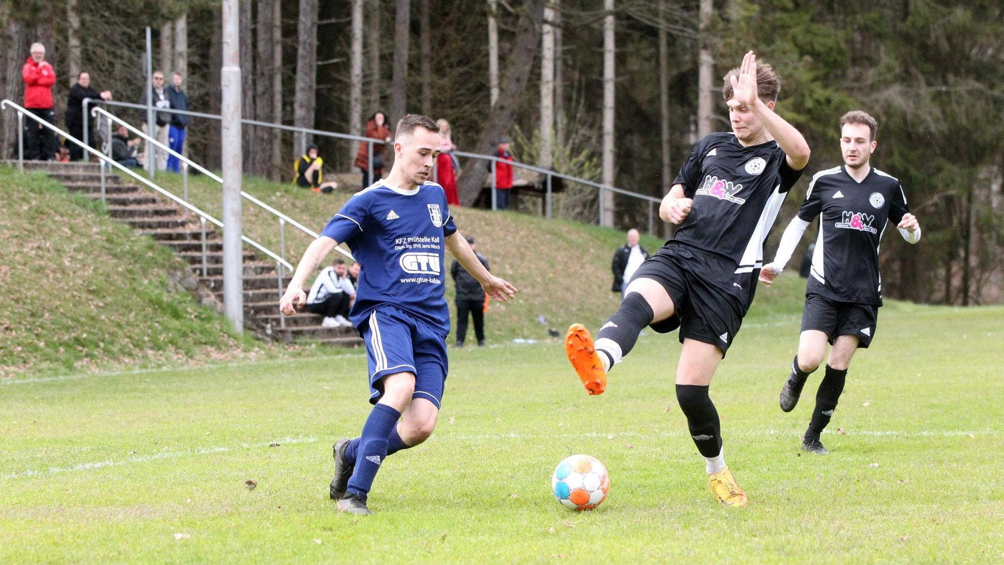 Maurice Gölden versucht sich den Ball am mit gestrecktem Bein heraneilendem Stotzheimer Spieler vorbeizulegen.