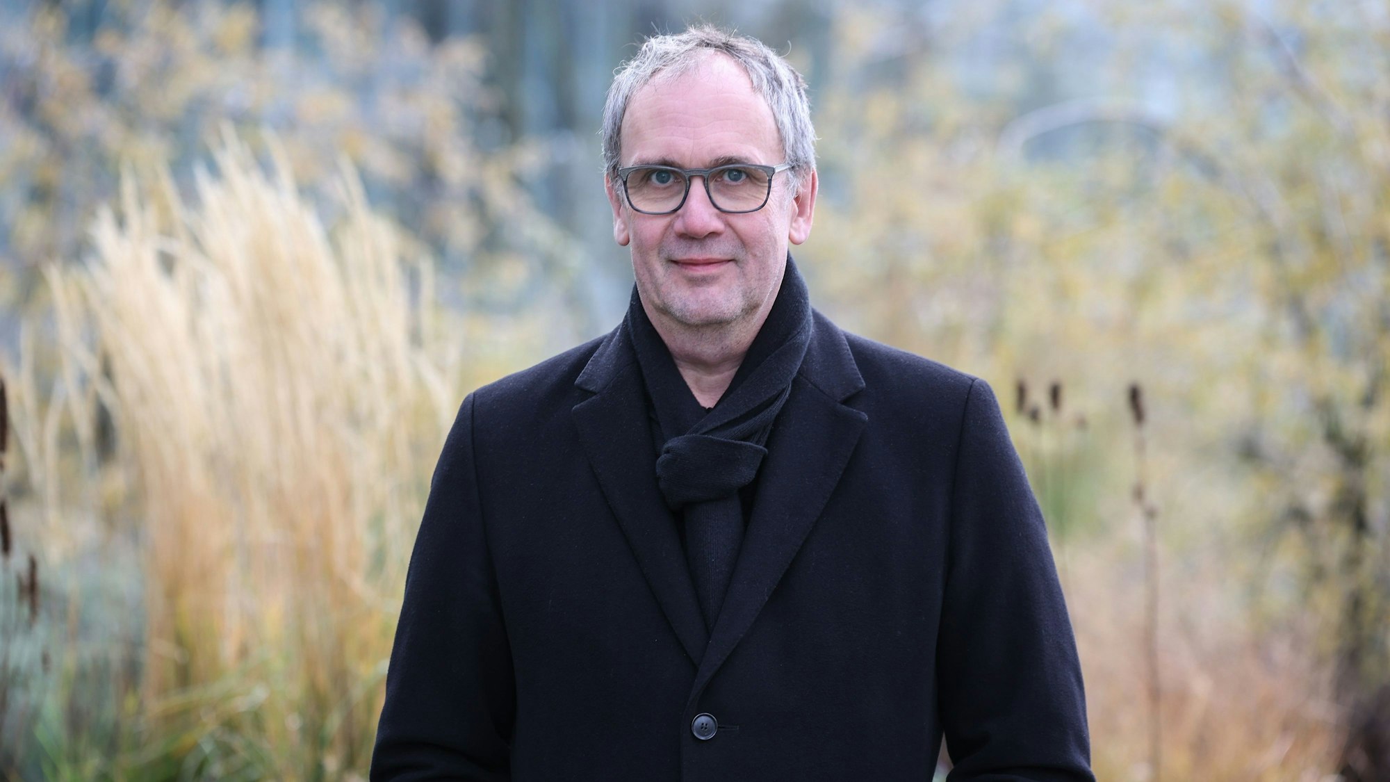 Bestseller-Autor Volker Kutscher steht im Mantel vor hohem Gras.