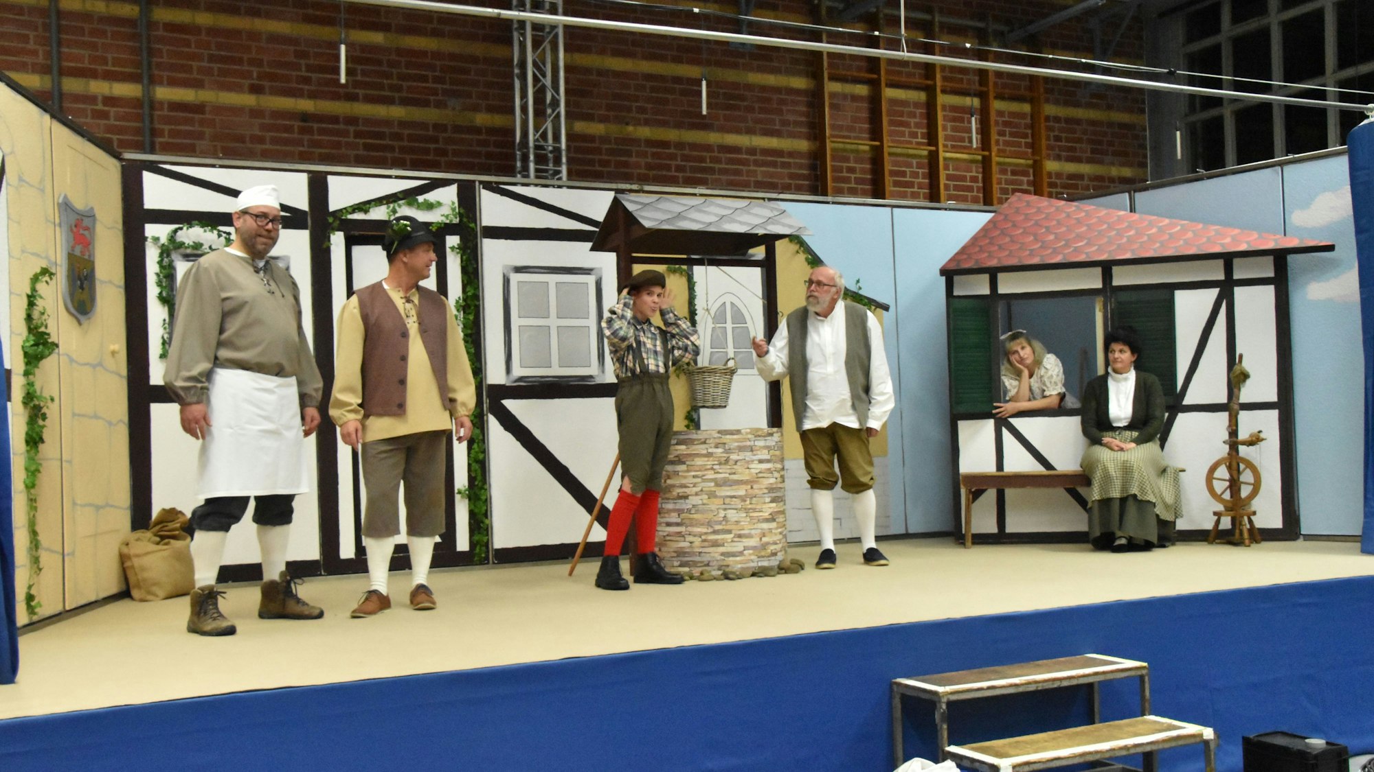 Schauspieler stehen für das Stück Frau Holle auf der Bühne, die einen Dorfplatz mit Brunnen darstellt.