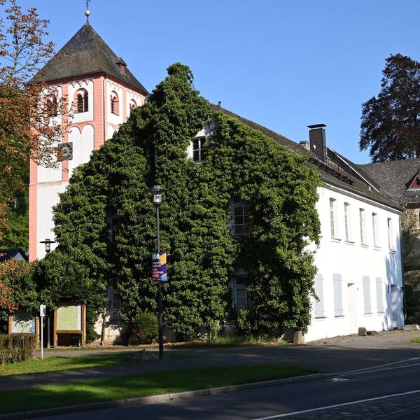 Das efeubewachsene Gebäude der Alte Kaplanei in Odenthal. Dahinter der Kirchturm von St. Pankratius.