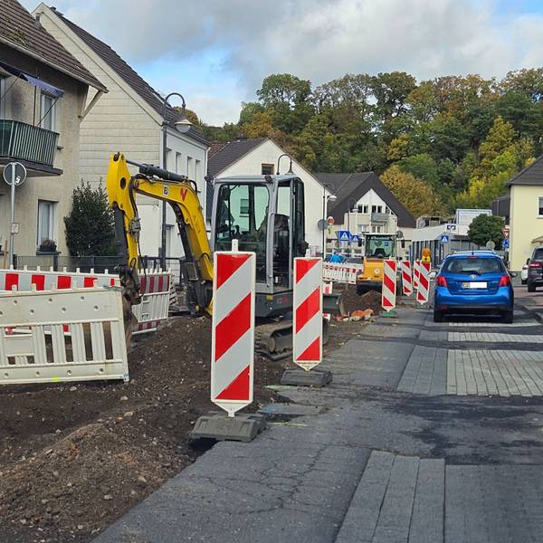 Zu sehen ist eine von Baggern aufgerissene Straßenhälfte, die mit Warnbaken abgesperrt ist, und eine Seite, auf der Autos fahren.