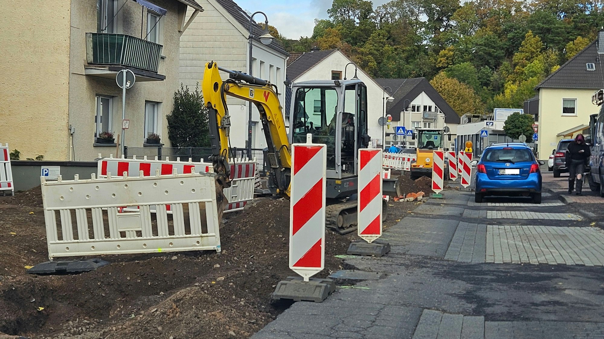 Zu sehen ist eine von Baggern aufgerissene Straßenhälfte, die mit Warnbaken abgesperrt ist, und eine Seite, auf der Autos fahren.