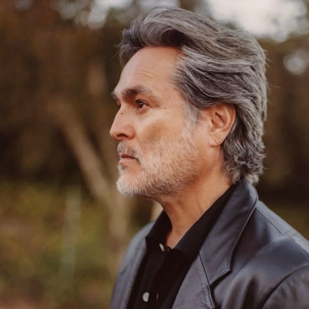 Eddie Chacon schaut im Profil nach links. Seine Haare sind grau und nach hinten gekämmt, sein kurz gestutzter Vollbart ist weiß.