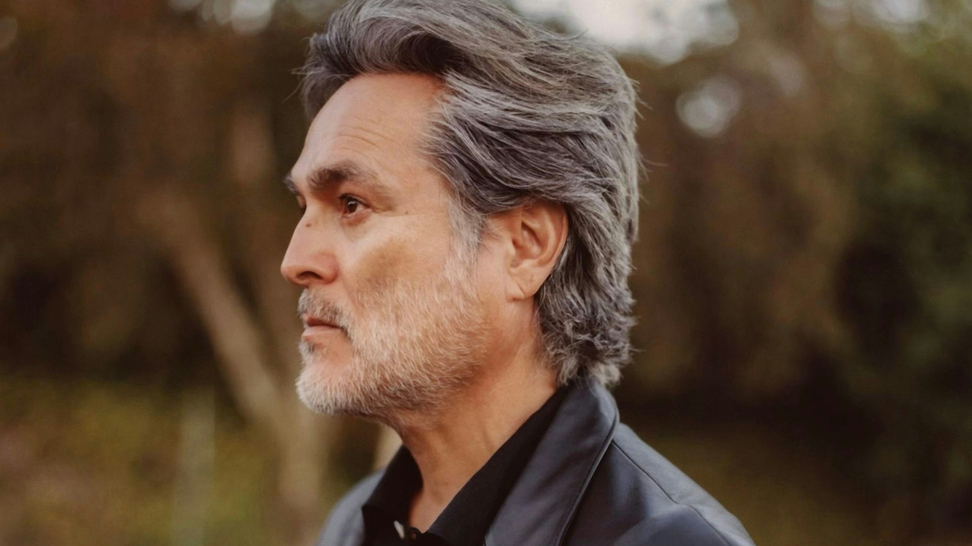 Eddie Chacon schaut im Profil nach links. Seine Haare sind grau und nach hinten gekämmt, sein kurz gestutzter Vollbart ist weiß.