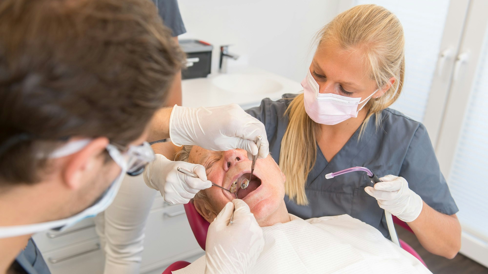 Ein Zahnarzt und eine Helferin versorgen einen Patienten nach den Regeln der Kunst.