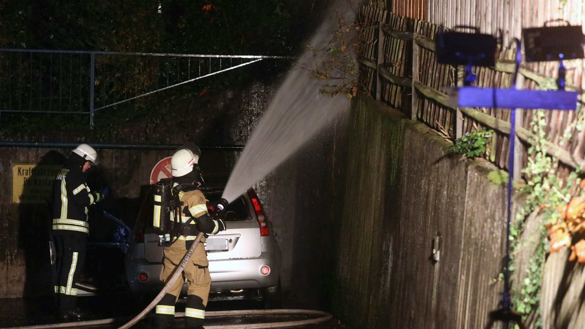 An der Linzer Straße in Bad Honnef brannte ein Auto. Das Feuer setzte auch eine Hecke sowie einen Zaun in Brand. Feuerwehrleute löschen die letzten Glutnester.