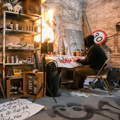 Eine Figur im Kapuzenpulli sitzt an einem Schreibtisch.