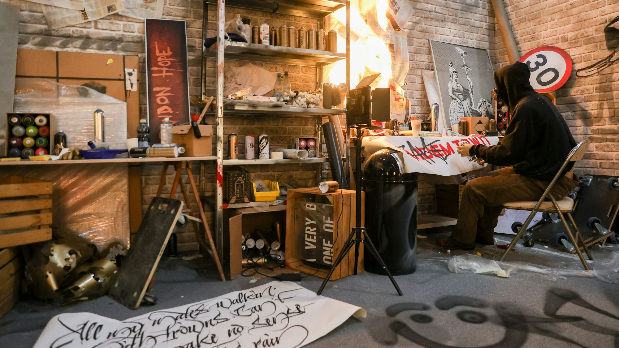 Eine Figur im Kapuzenpulli sitzt an einem Schreibtisch.